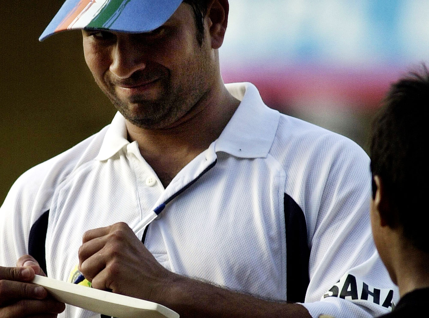 Sachin Tendulkar smiles while signing an autograph for a young fan