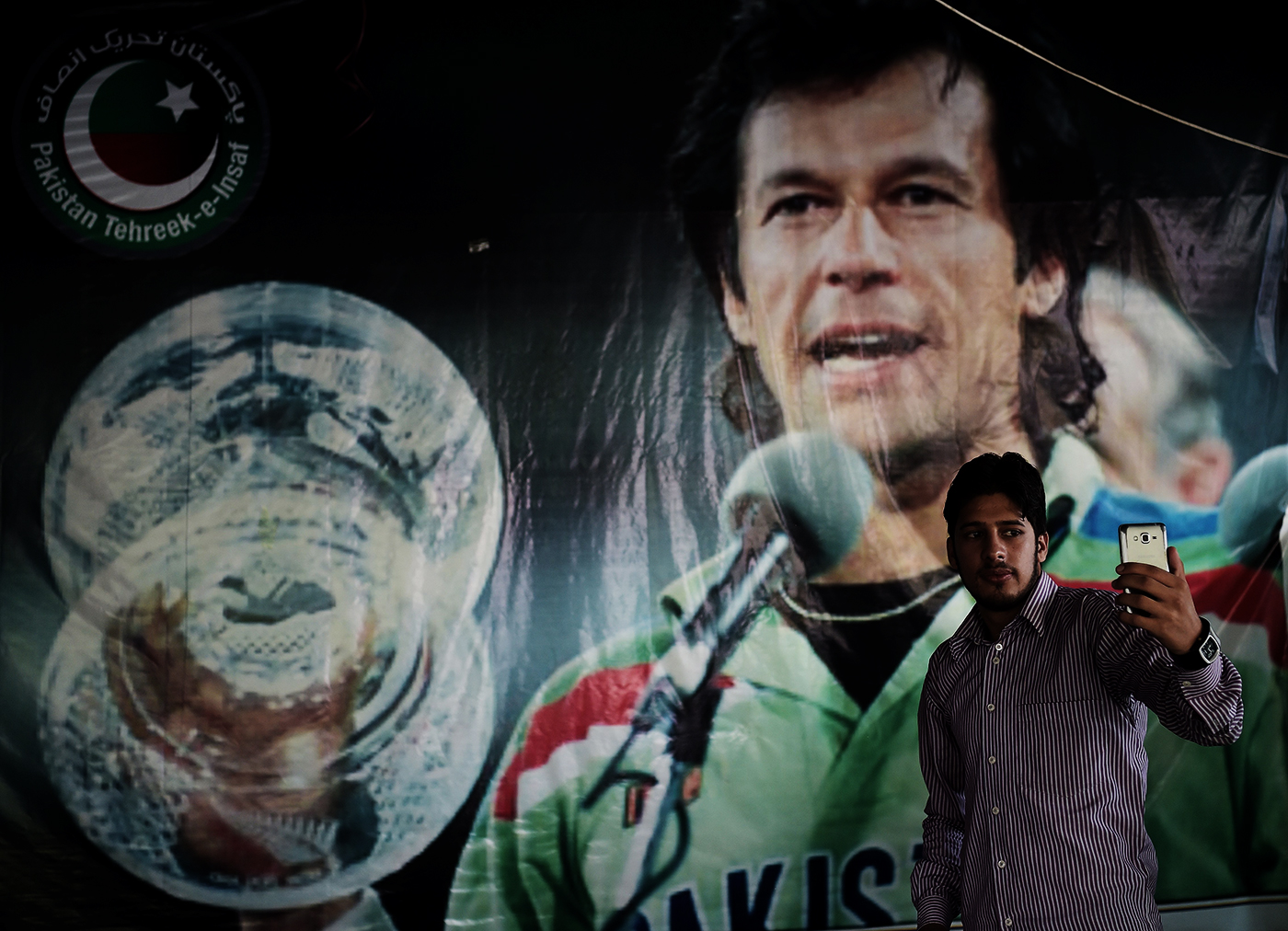 A man take a photo with a poster of Imran Khan in the background